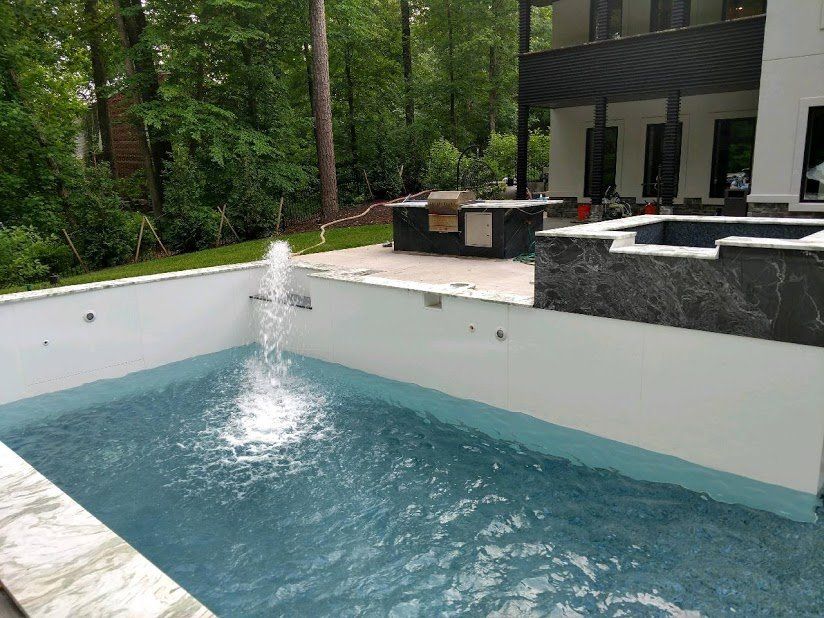 A large swimming pool with a fountain in the middle of it in front of a house.