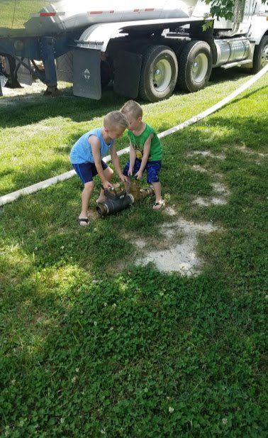 Two young boys are playing in the grass in front of a truck.