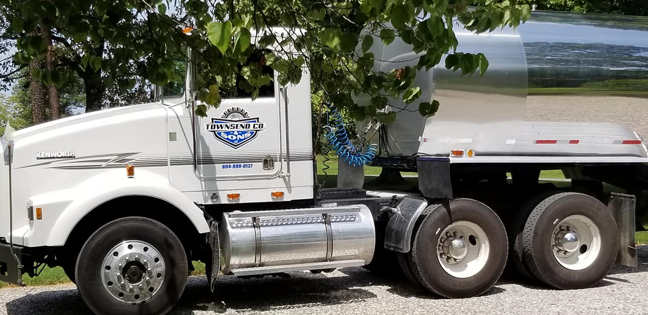 A white semi truck is parked in a gravel lot next to a tree.