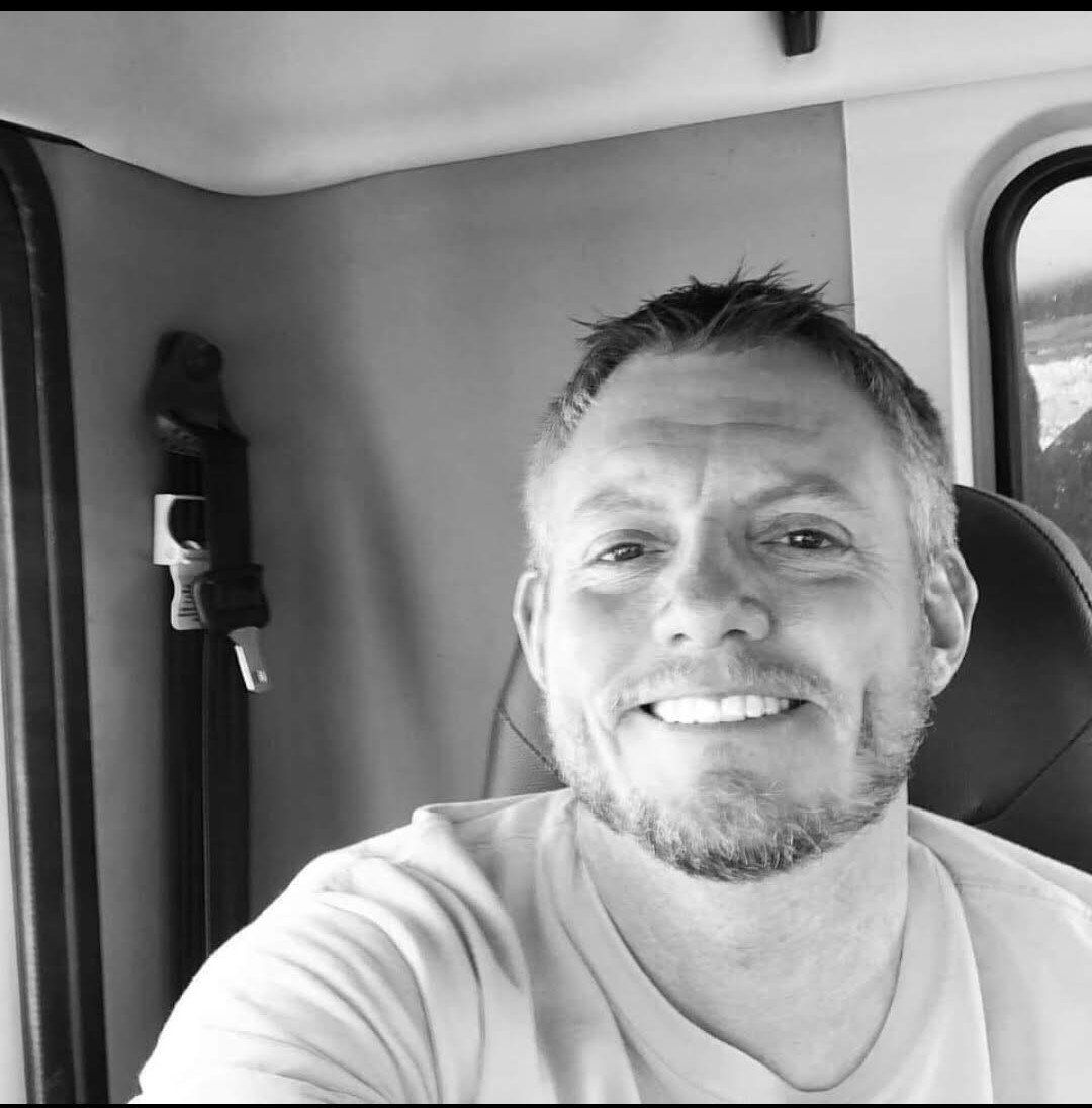 A man with a beard is smiling in a black and white photo.