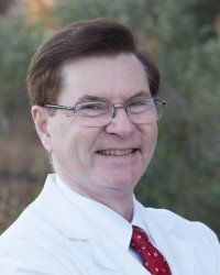 A man in a white coat and red tie is smiling for the camera.