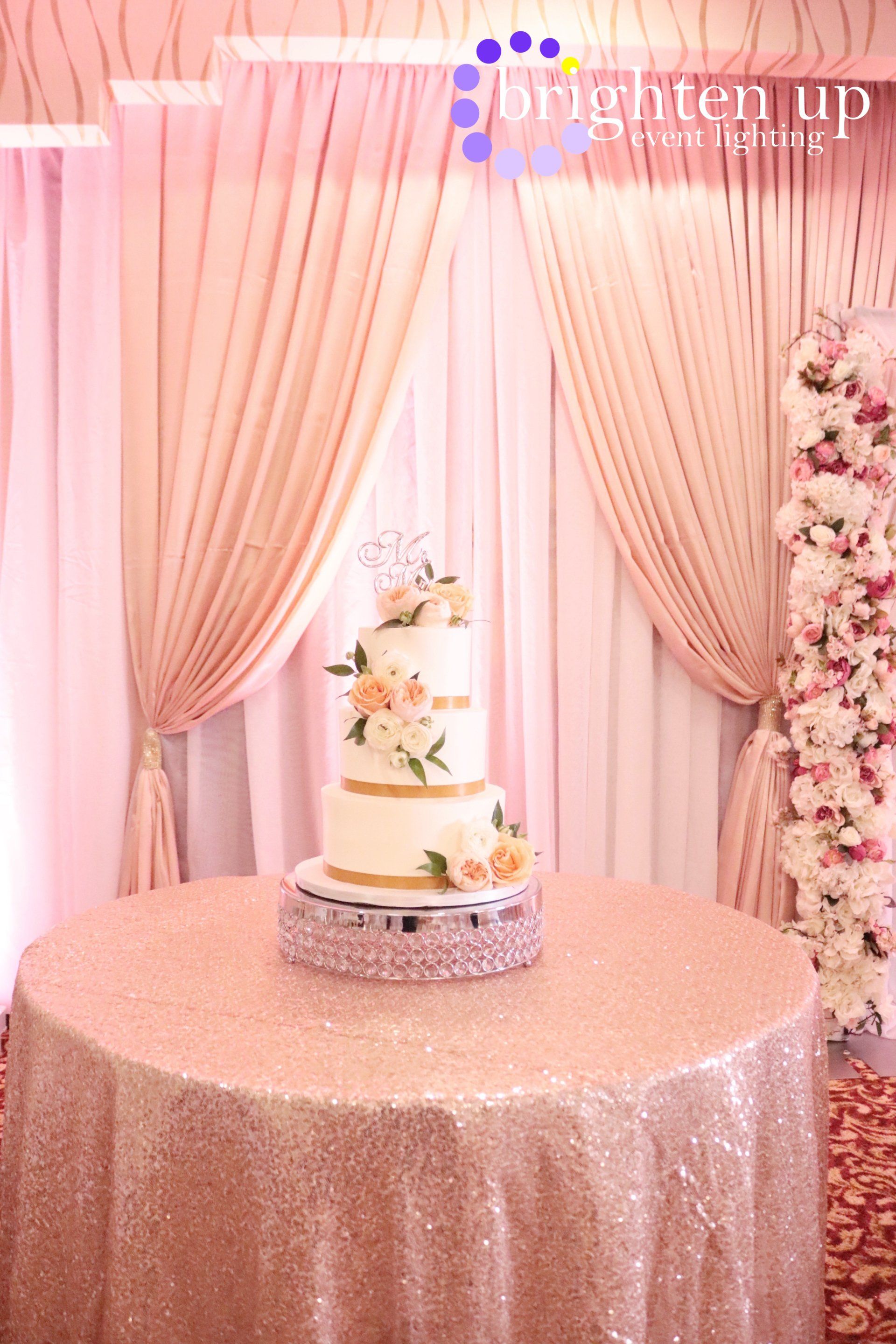 A wedding cake is sitting on a table in front of a pink curtain.