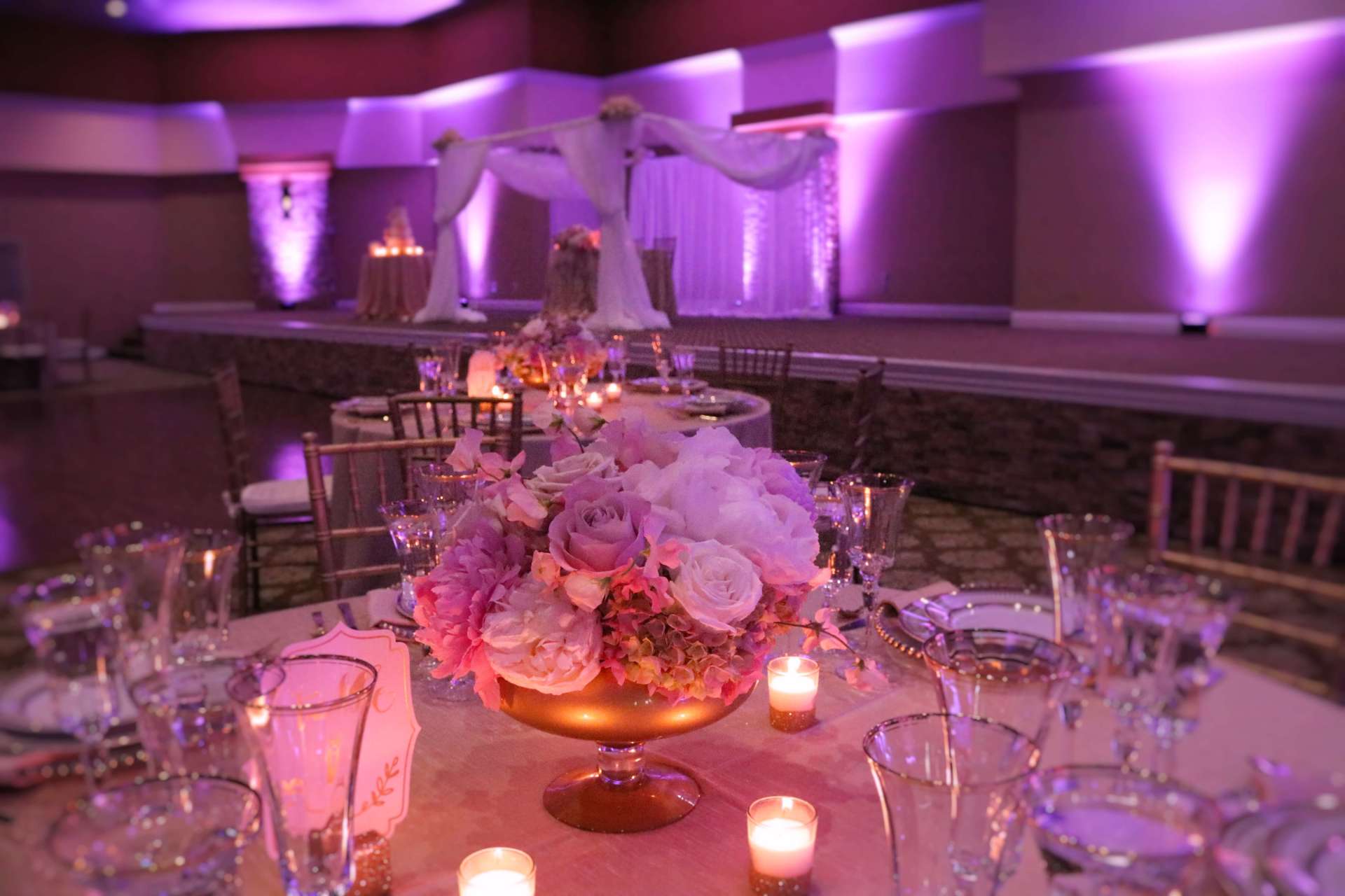 A table set for a wedding reception with a vase of flowers and candles on it.