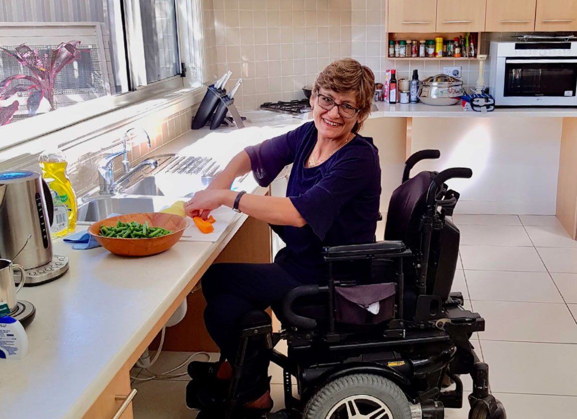 A woman in a wheelchair is sitting at a counter in a kitchen.