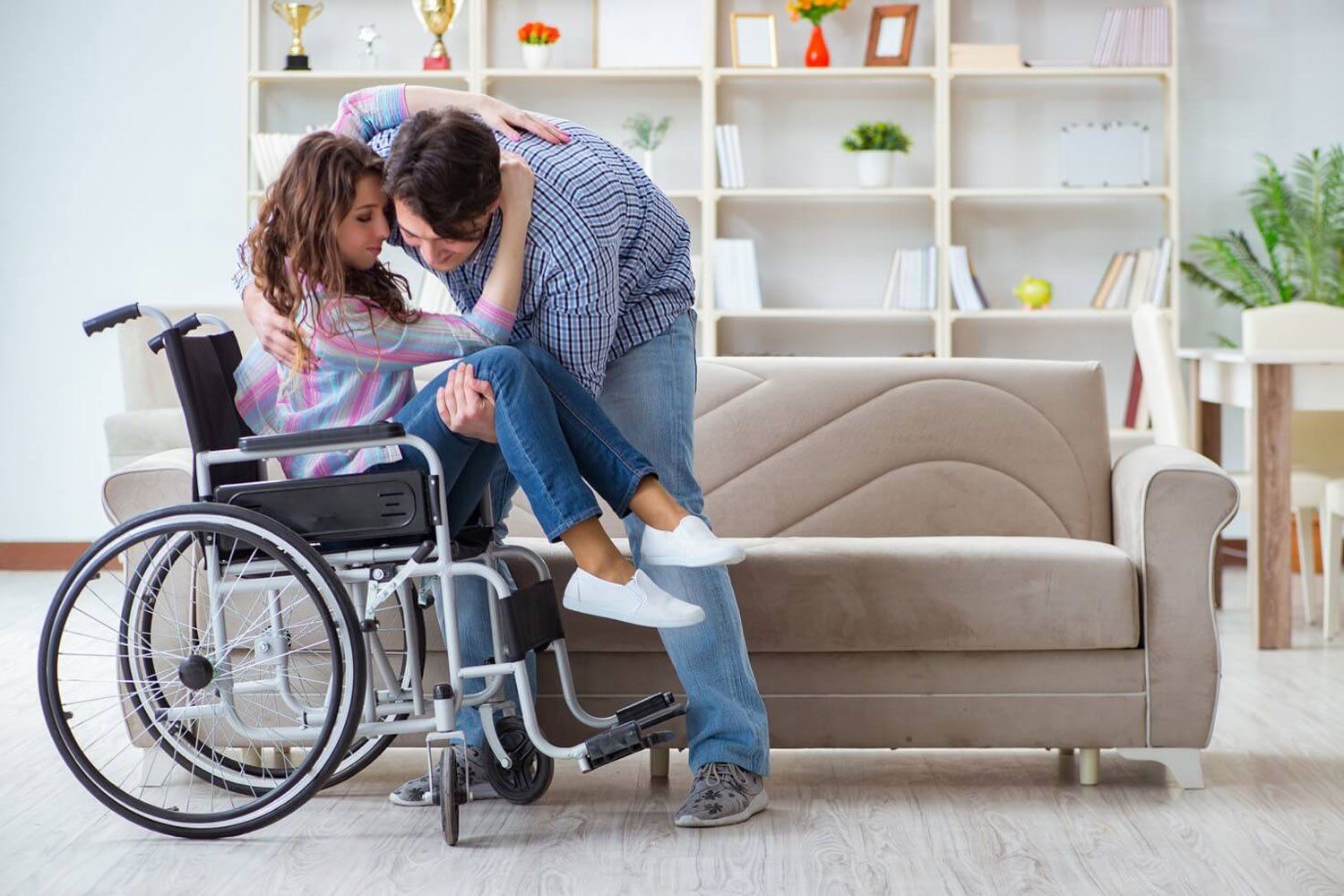 A man is carrying a woman in a wheelchair in a living room.