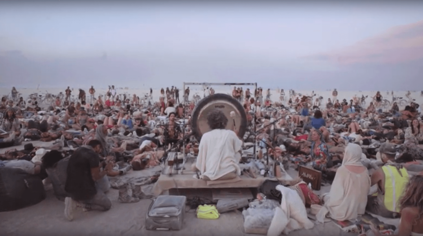 A man is playing a gong in front of a crowd of people.