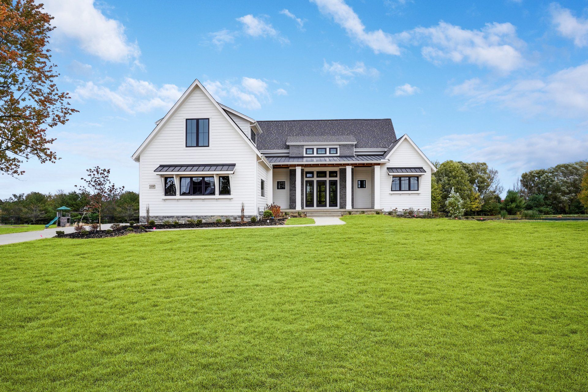 A large white house sits in the middle of a lush green field