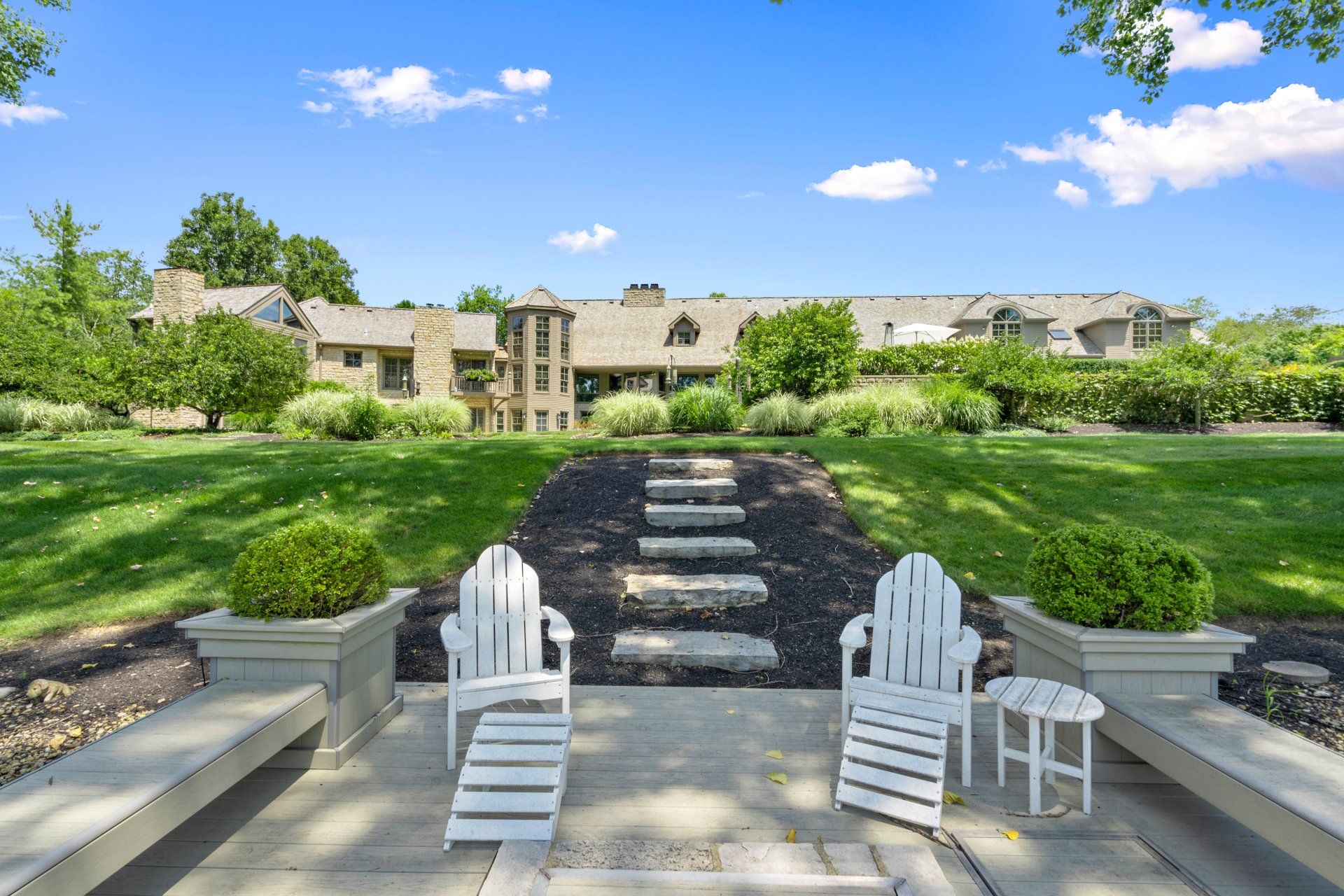 Two white chairs sit on a patio in front of a large house