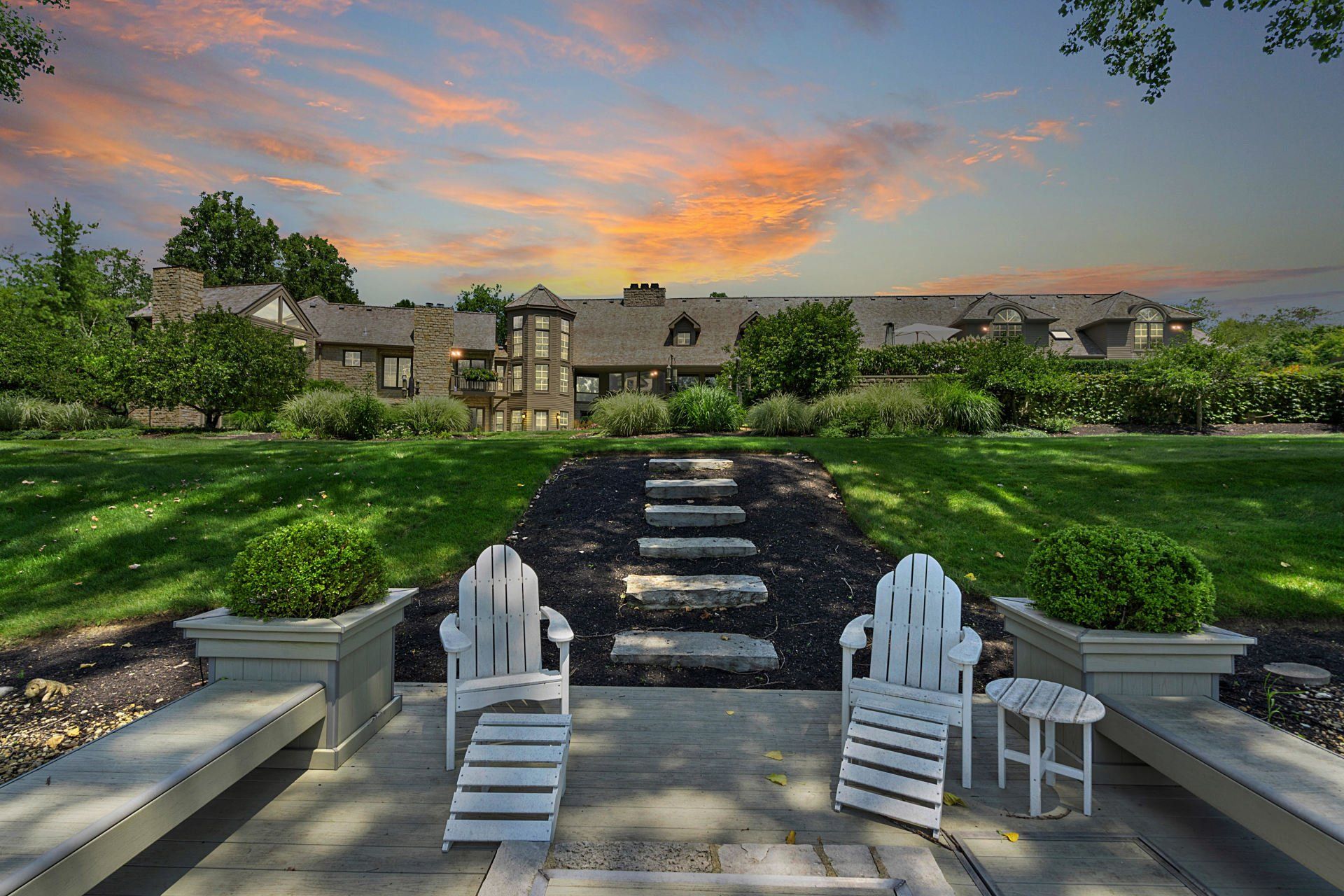 Two white chairs sit on a patio in front of a large house