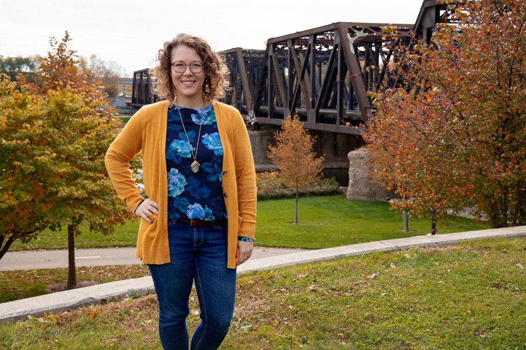 A woman in a yellow cardigan is standing in front of a bridge.
