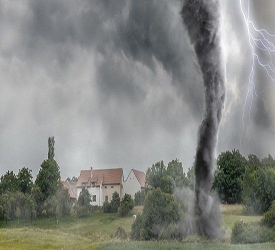 Dark tornado touching down in a rural field near houses, with lightning in a stormy sky.