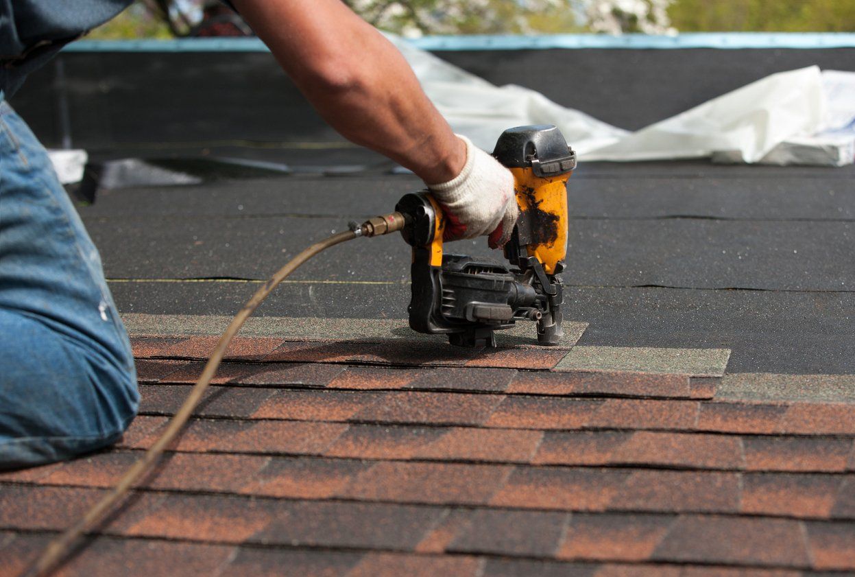 Worker using a roofing nail gun to install shingles on a roof