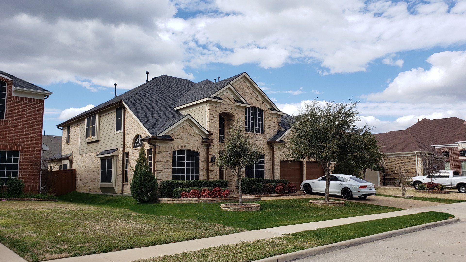 Suburban house with stone facade, front lawn, and parked white SUV under a partly cloudy sky
