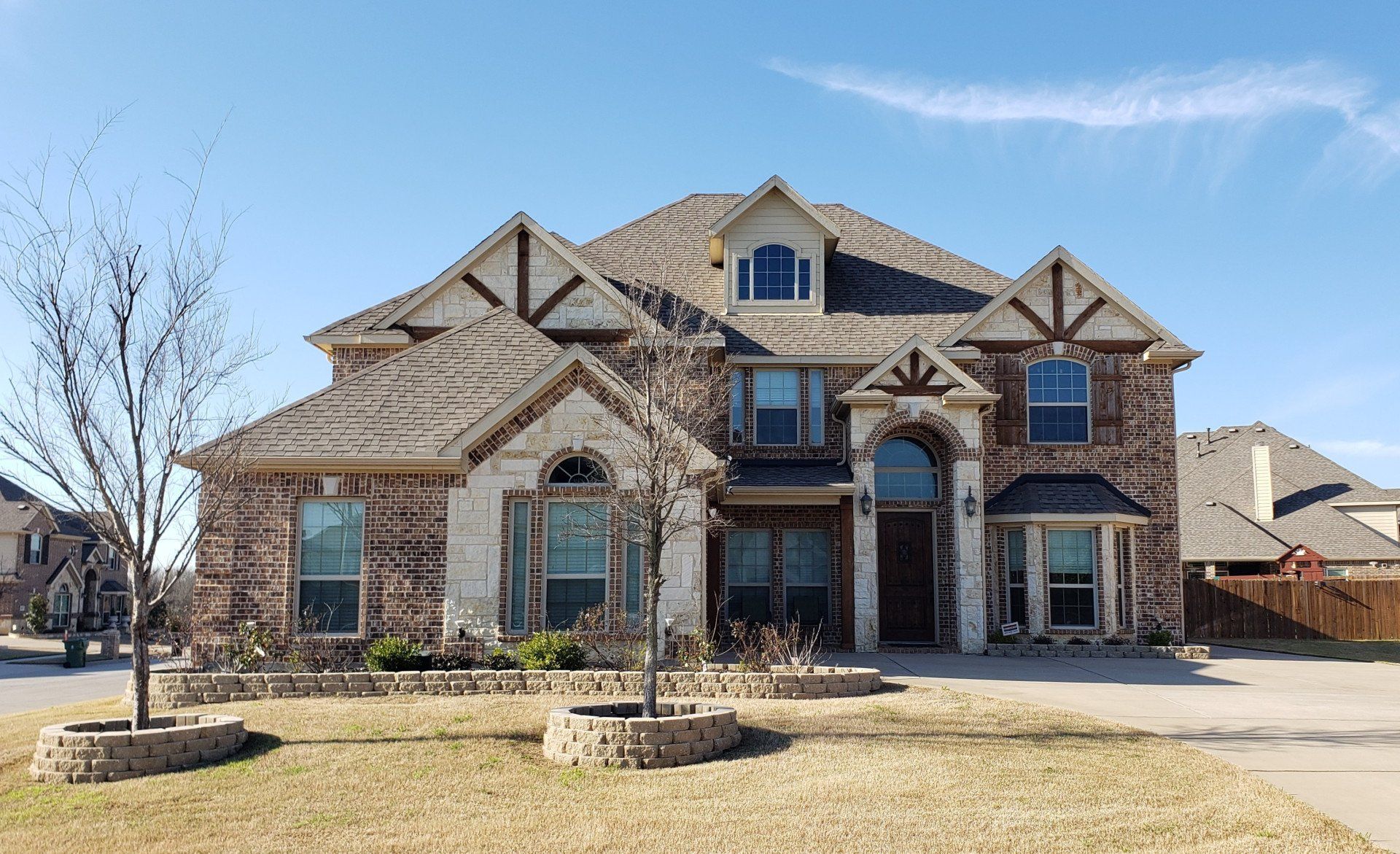 Two-story brick suburban house with arched windows, gabled roof, and a front driveway on a clear day