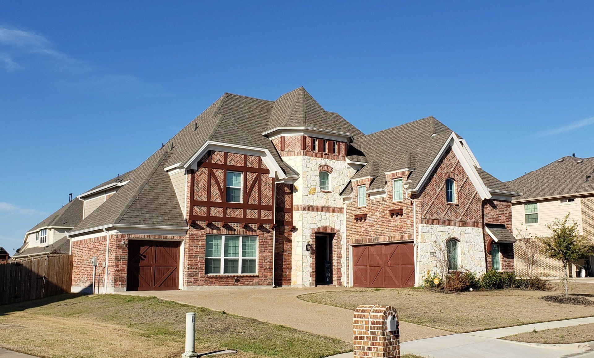 Large two-story stone and brick suburban house with a dark shingled roof and front lawn