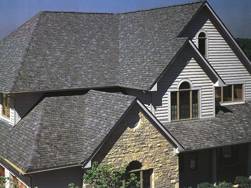 Suburban house with gray shingled roof and stone exterior under a clear blue sky