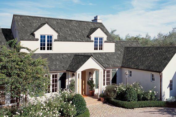 White two-story house with dark roof, front garden, and driveway under a clear sky