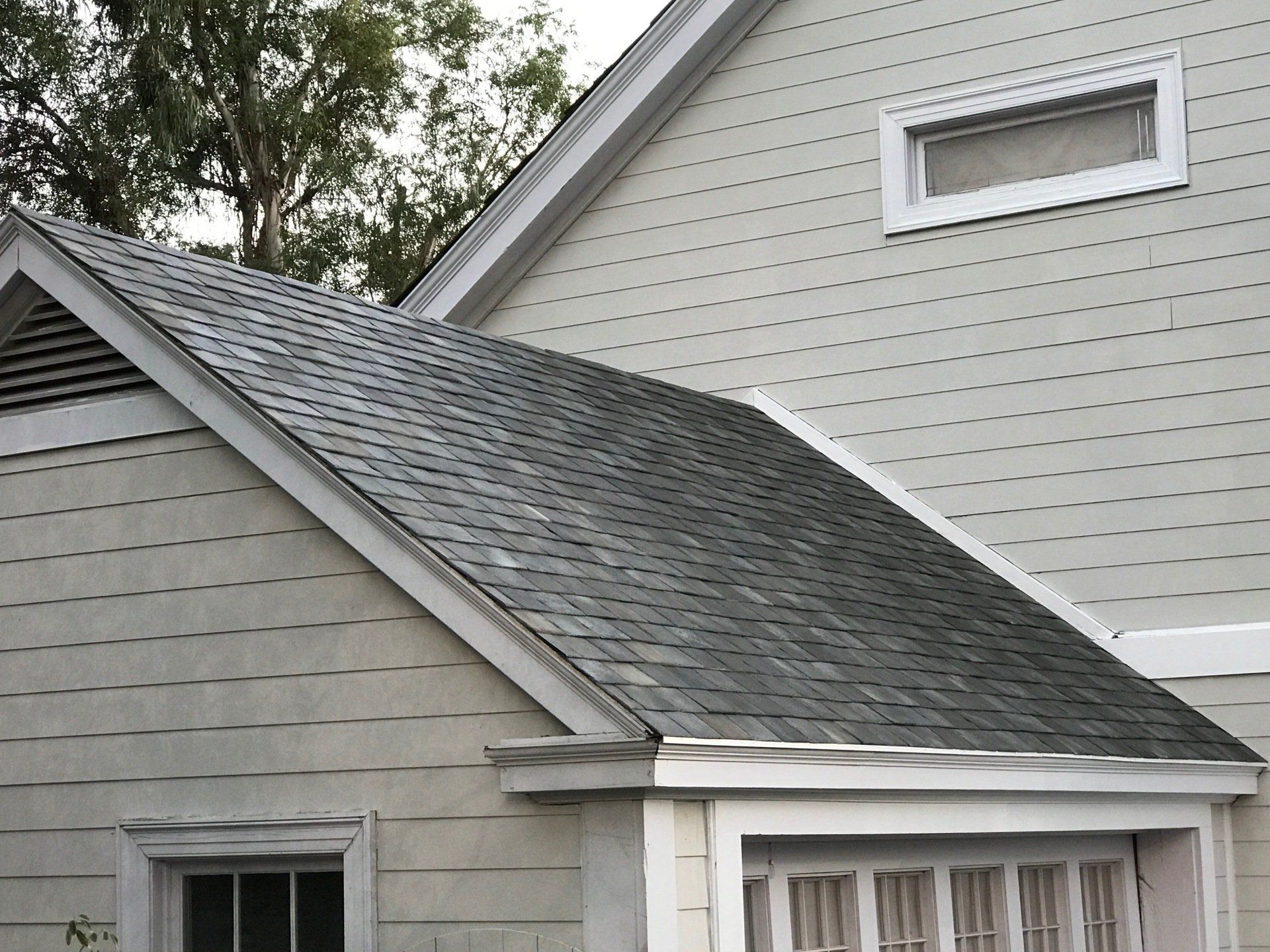 Gray house roof with dark shingled dormer and white trim under trees