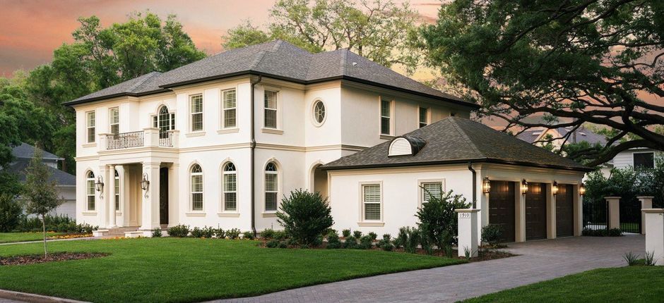Large white two-story house with a dark roof, arched windows, and a manicured lawn at sunset