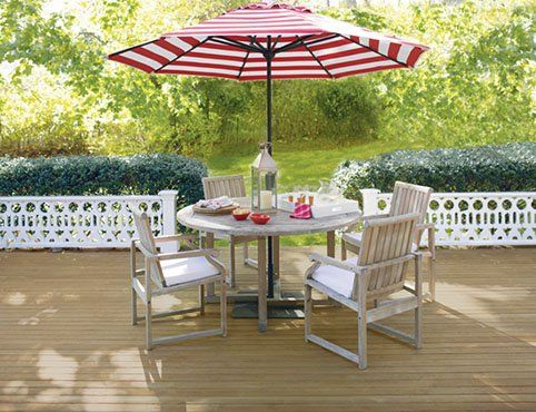 Patio table and chairs under a red and white striped umbrella on a wooden deck.