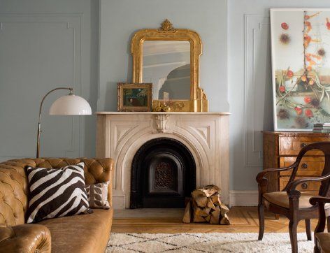 Living room with fireplace, gold mirror, tan leather sofa, and floral artwork.