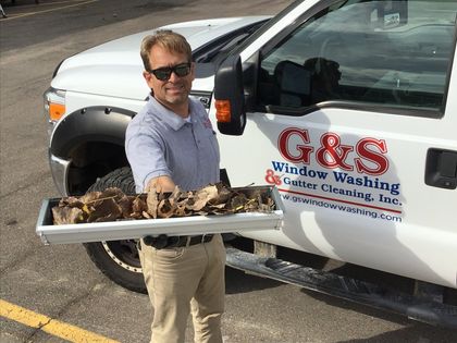 A man is holding a tray of leaves in front of a g & s window washing truck.