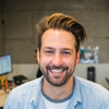 A man with a beard is smiling and wearing a blue shirt