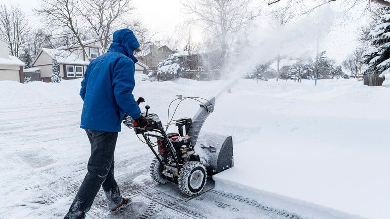 A man is using a snow blower to clear snow from his driveway.