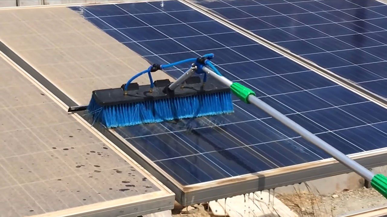 A person is cleaning a solar panel with a broom
