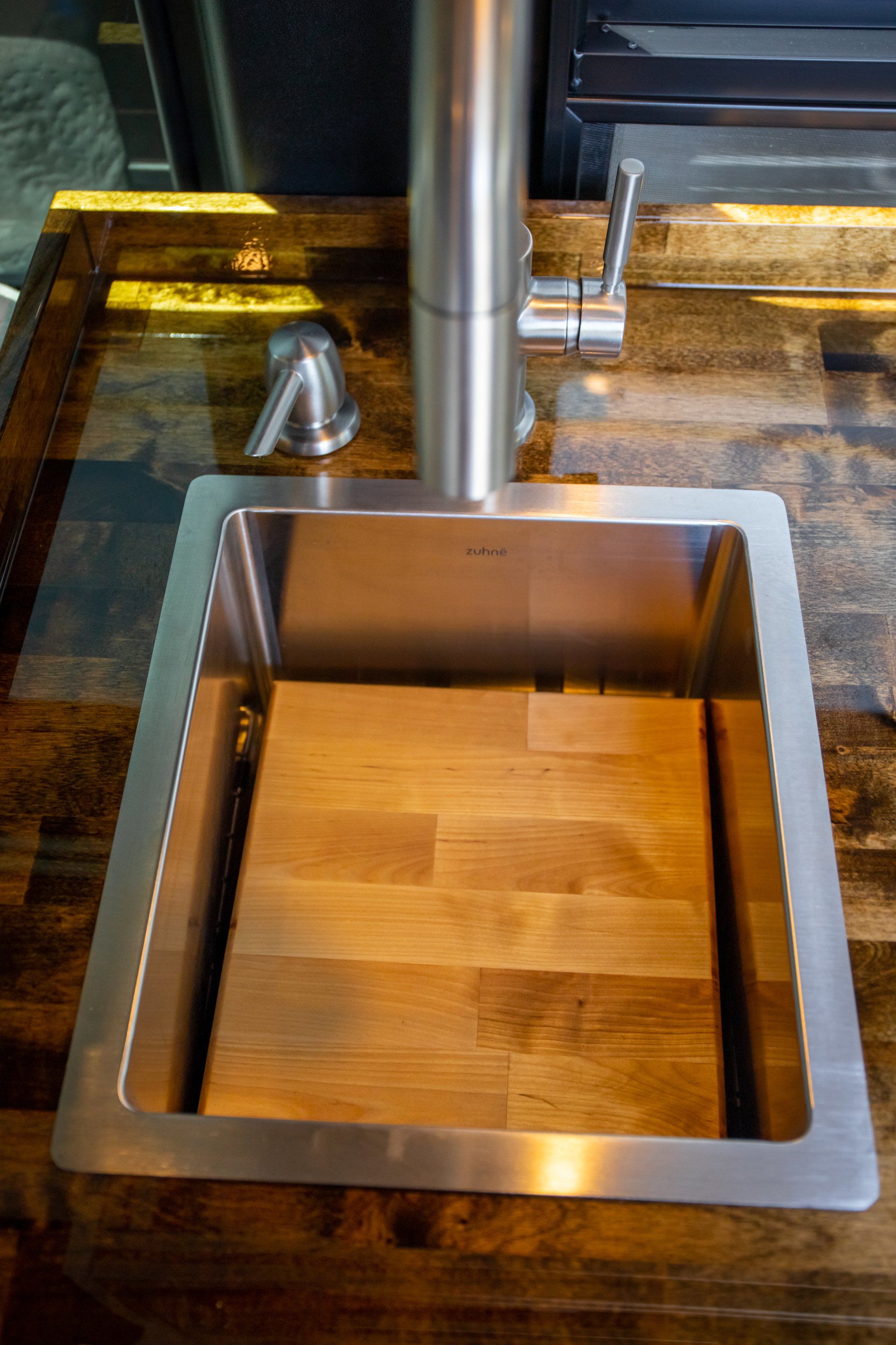 a stainless steel sink with a wooden cutting board underneath it .
