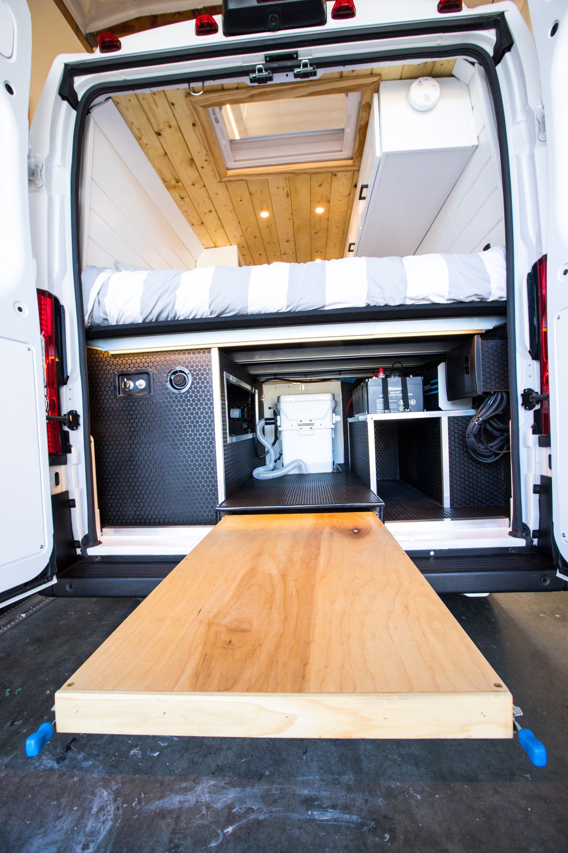 the back of a van with a bed and a wooden table .