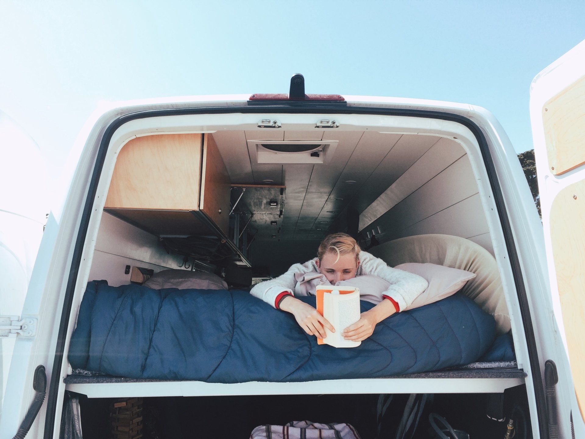 a woman is laying in the back of a van reading a book .