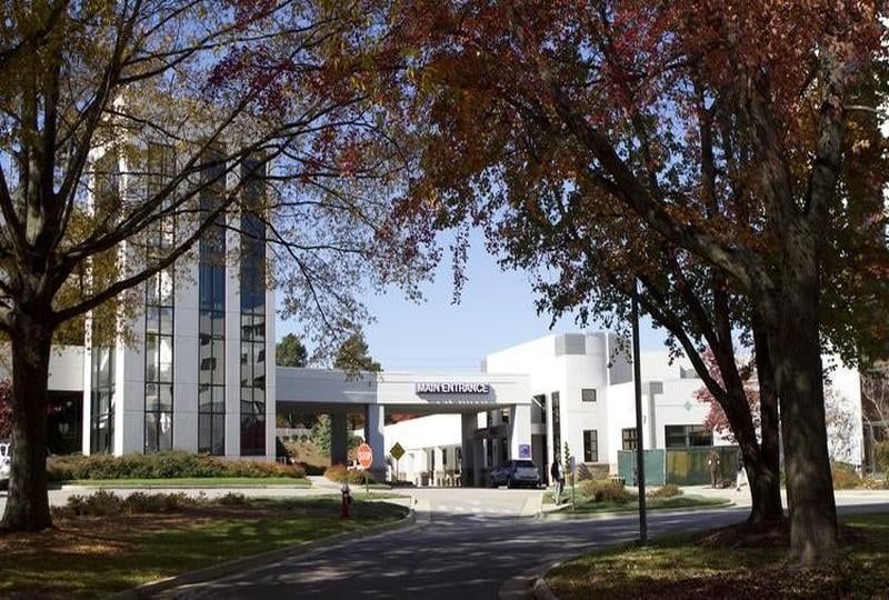 Hospital entrance under autumn trees; white building with sign, driveway.