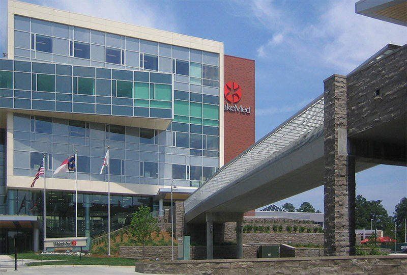 Modern building with glass windows, red logo, and walkway bridge on a sunny day.