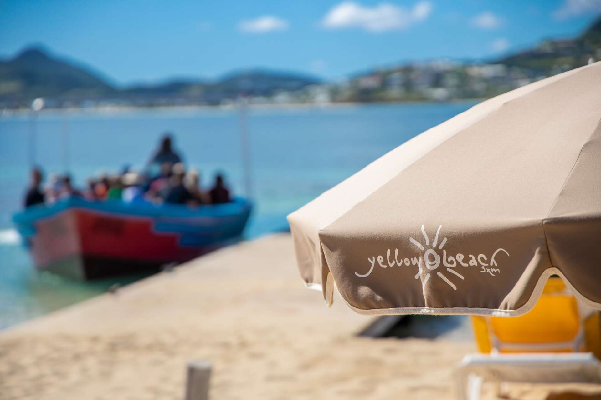 An umbrella on a beach with a boat in the background