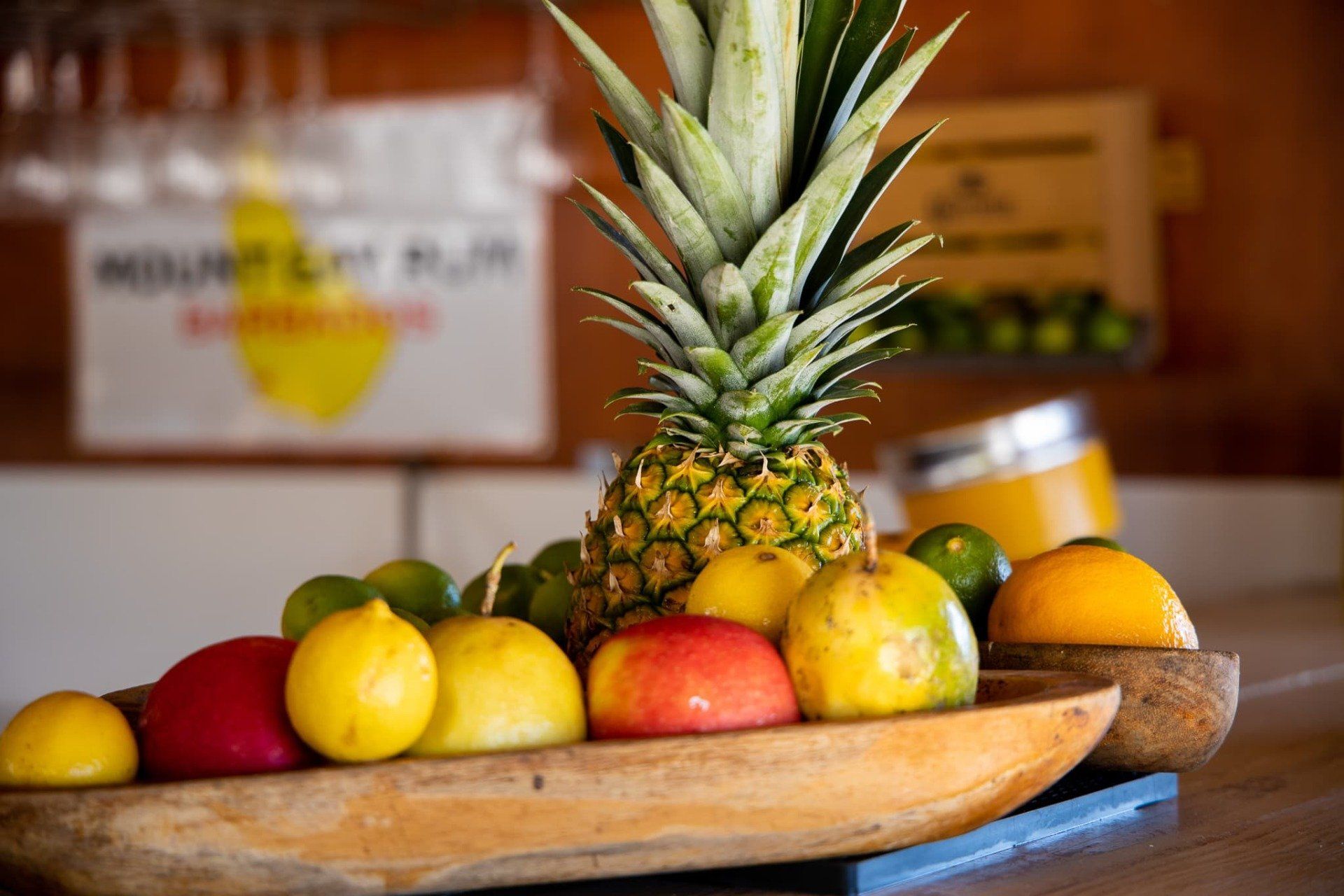 A wooden bowl filled with fruit and a pineapple on a table.