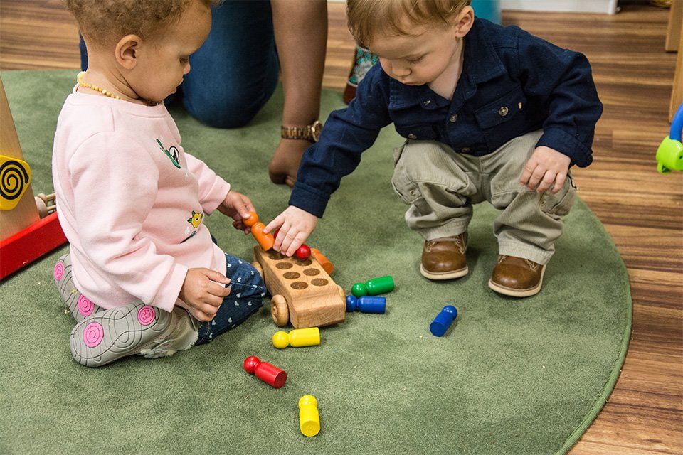 A boy and a girl are playing with wooden toys on the floor.