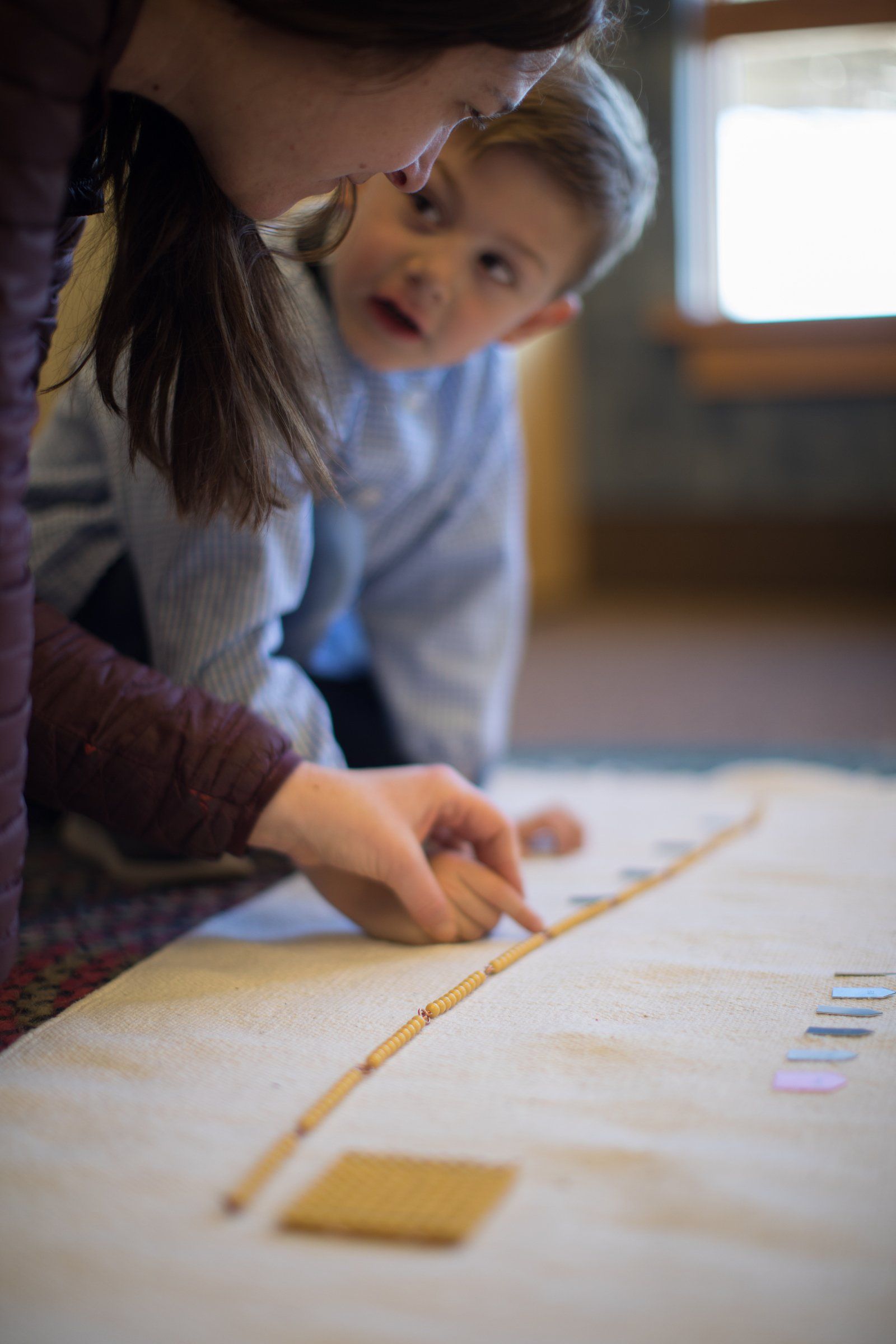 A montessori guide and a child are looking at montessori math materials
