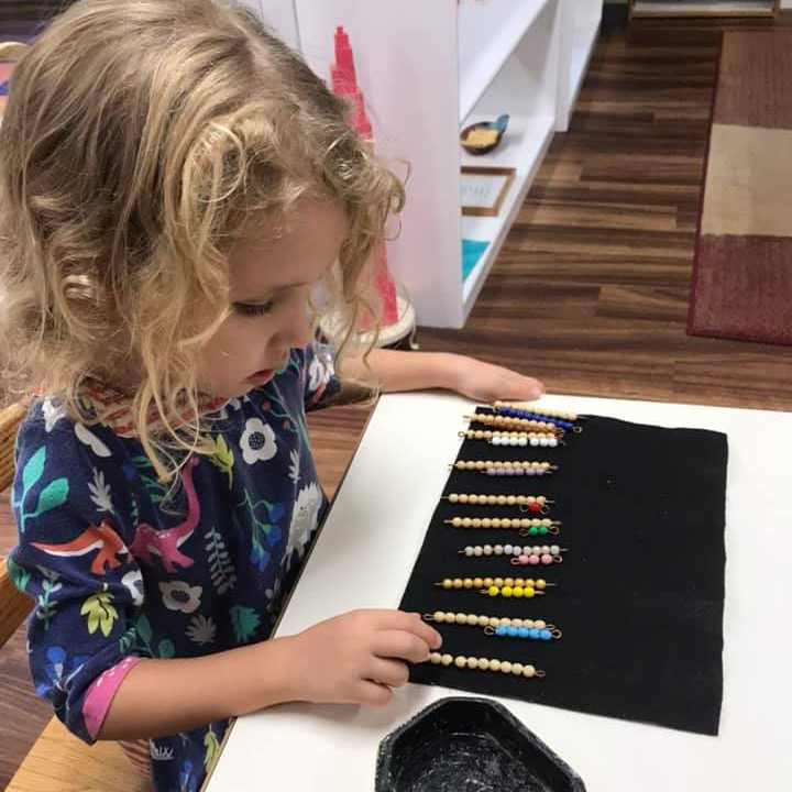 A little girl is sitting at a table working with montesori math beads