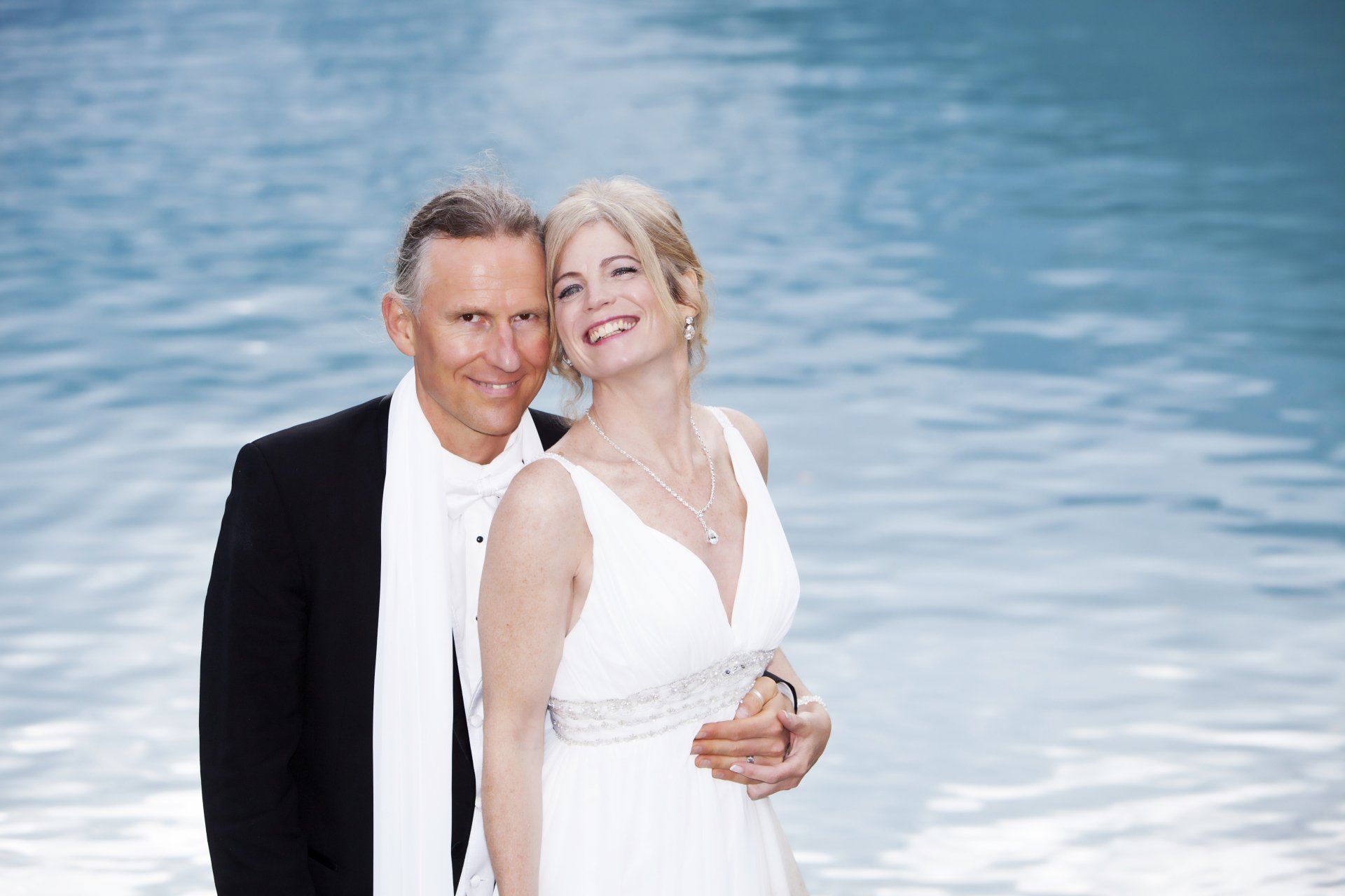 A bride and groom are posing for a picture in front of a body of water.