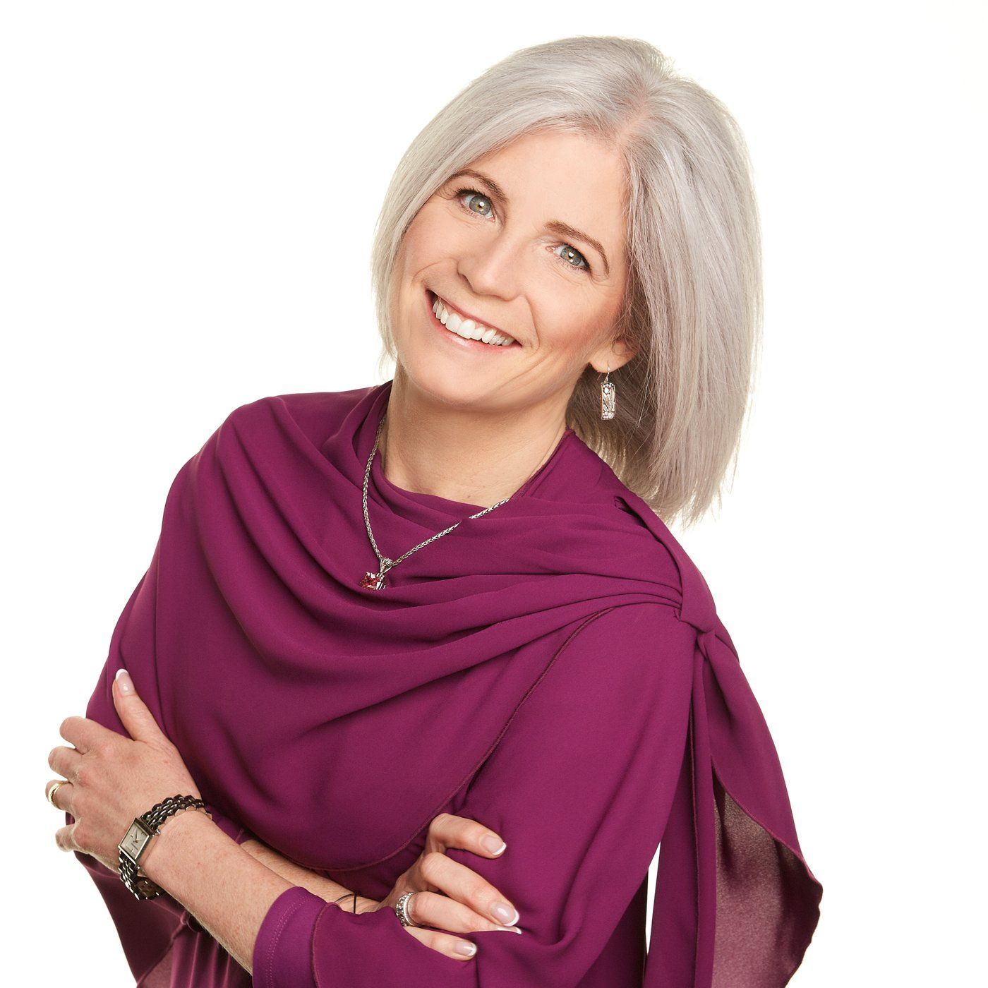 A woman wearing a purple top and a necklace smiles for the camera