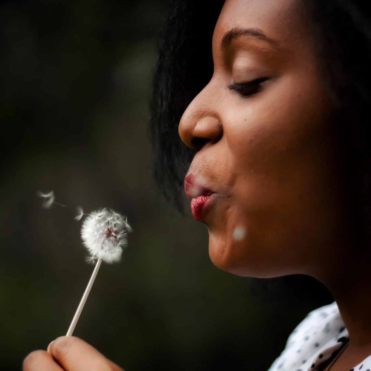 A woman blowing a dandelion with her mouth