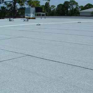 Flat commercial roof, light gray color, with visible seams and vents. Sky in the background.