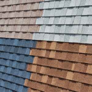 Close-up view of a roof with shingles in four different color sections: tan, gray, brown, and blue.