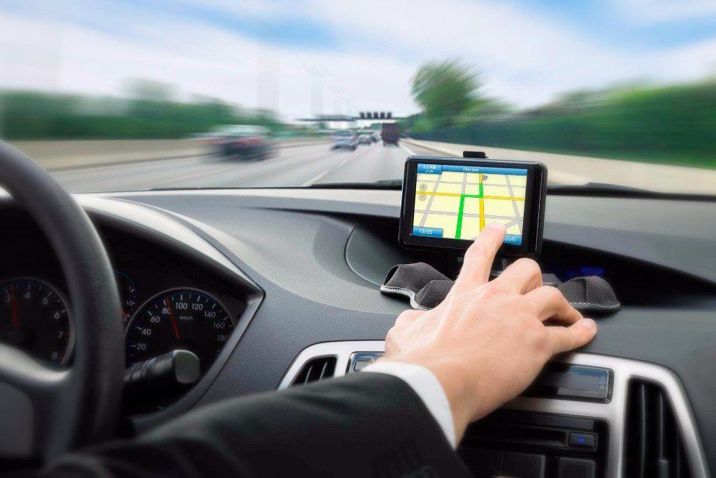 A man is driving a car and pointing at a map on the dashboard.