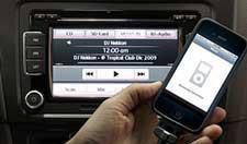 A person is holding a cell phone in front of a car radio.