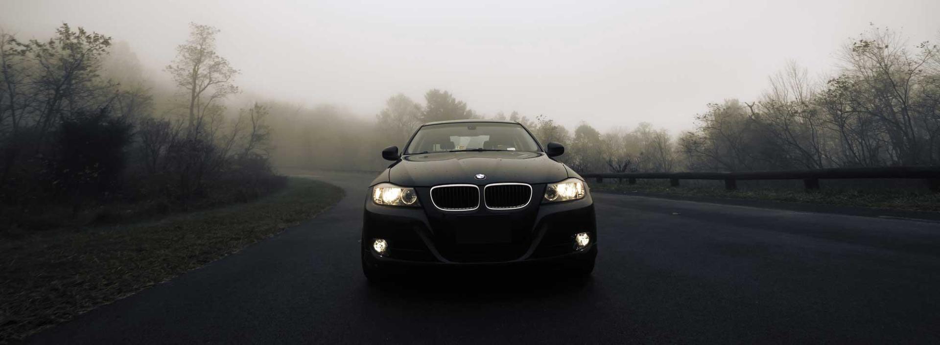 A black car is driving down a foggy road.