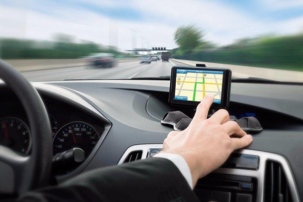 A man is driving a car and pointing at a map on the dashboard