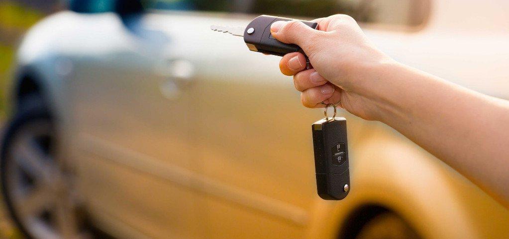 A person is holding a car key in front of a car.