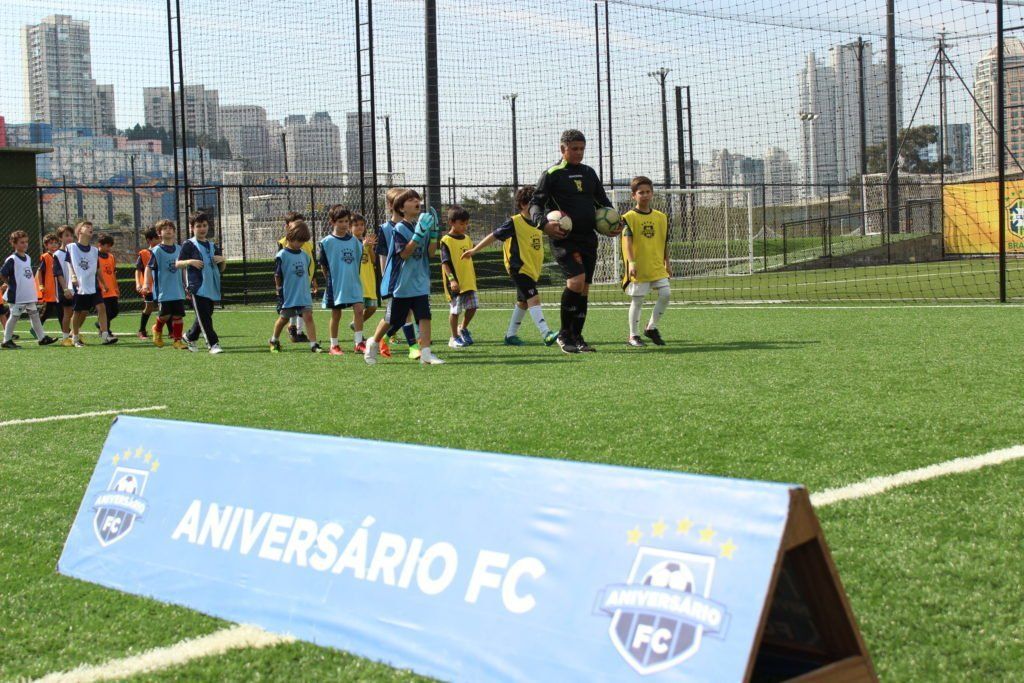 Jogadores de futebol e treinador em um campo verde. Faixa com o nome 